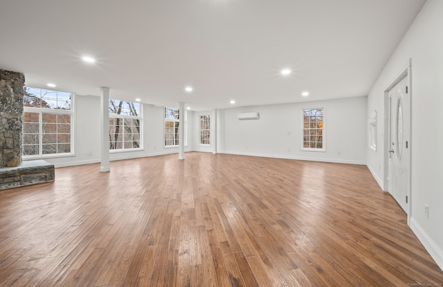 unfurnished living room featuring a wall mounted AC, a fireplace, and light hardwood / wood-style flooring