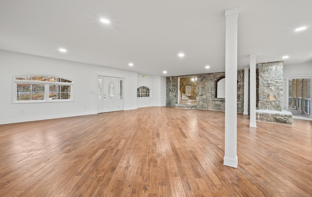 unfurnished living room featuring a stone fireplace, light wood-type flooring, and decorative columns