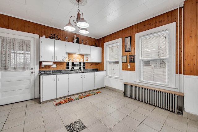 kitchen with radiator heating unit, hanging light fixtures, wooden walls, white cabinets, and an inviting chandelier