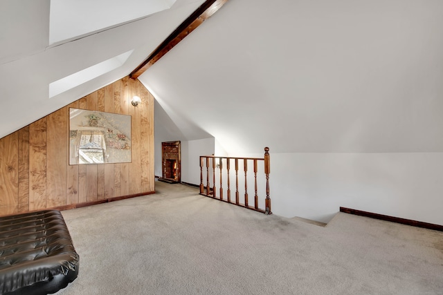 bonus room featuring lofted ceiling with skylight, wood walls, and light colored carpet