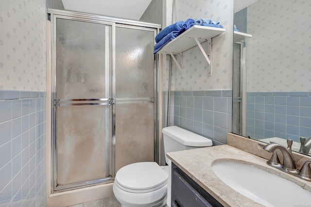 bathroom with a shower with door, vanity, toilet, and tile walls