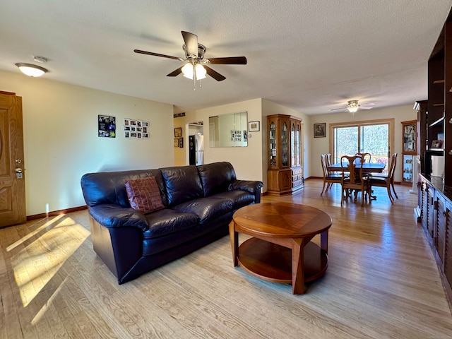 living room with ceiling fan, light wood-type flooring, and a textured ceiling