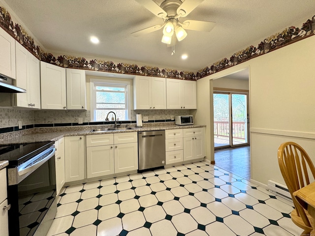 kitchen with light stone counters, stainless steel appliances, ceiling fan, sink, and white cabinetry