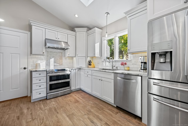 kitchen with appliances with stainless steel finishes, pendant lighting, white cabinets, and light hardwood / wood-style floors