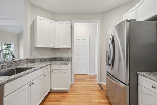 kitchen featuring appliances with stainless steel finishes, sink, white cabinets, light stone counters, and light wood-type flooring