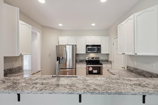 kitchen featuring white cabinetry, appliances with stainless steel finishes, a kitchen bar, and kitchen peninsula