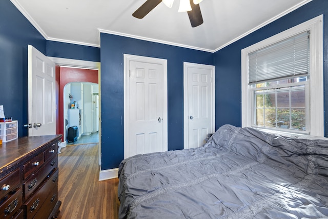 bedroom with dark wood-type flooring, ceiling fan, crown molding, and multiple closets