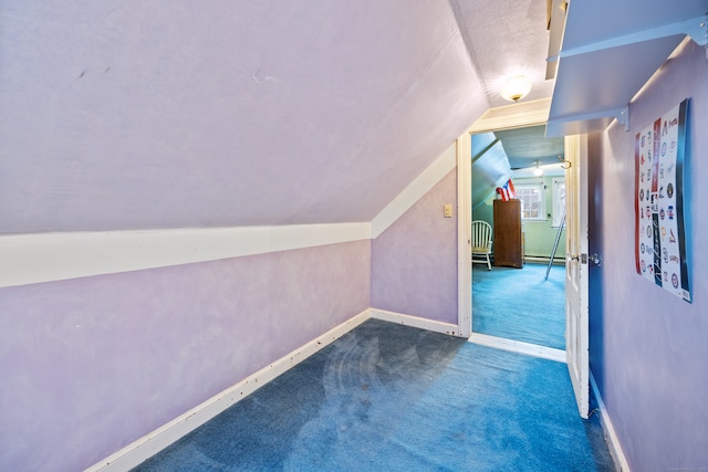 additional living space featuring baseboard heating, lofted ceiling, and dark colored carpet