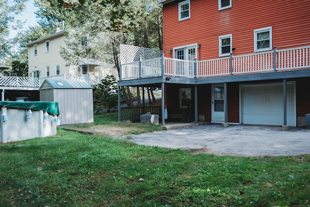 back of property featuring a wooden deck, a storage unit, a garage, and a lawn