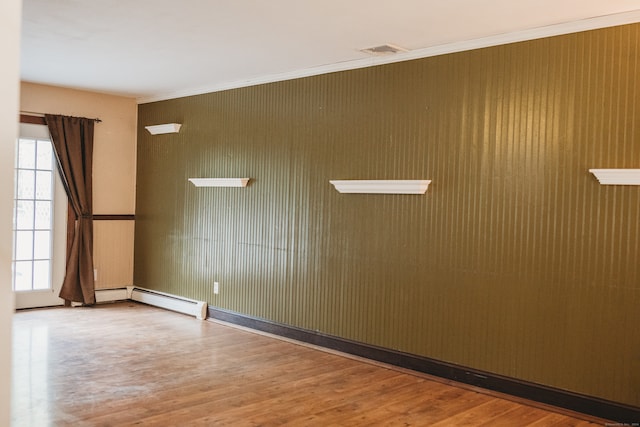 unfurnished room with a wealth of natural light, crown molding, a baseboard heating unit, and wood-type flooring