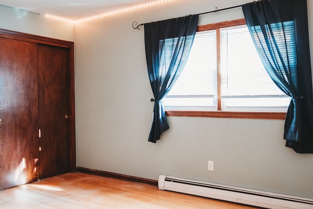 unfurnished room with a healthy amount of sunlight, a baseboard heating unit, and light wood-type flooring