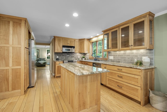 kitchen featuring light wood-type flooring, ornamental molding, appliances with stainless steel finishes, a kitchen island, and light stone counters