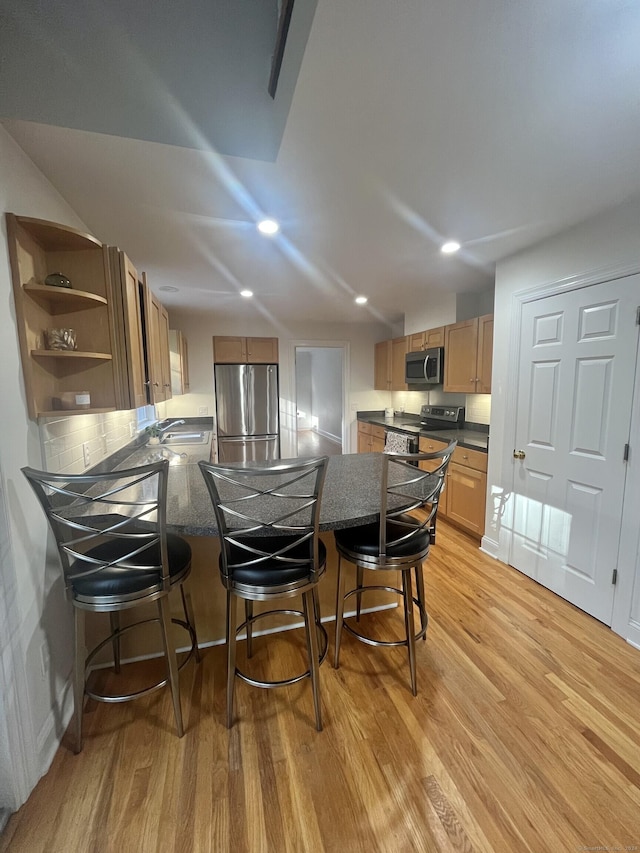 kitchen featuring stainless steel appliances, tasteful backsplash, light hardwood / wood-style flooring, kitchen peninsula, and a breakfast bar area