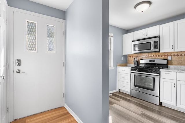 kitchen with white cabinetry, stainless steel appliances, decorative backsplash, and light wood-type flooring