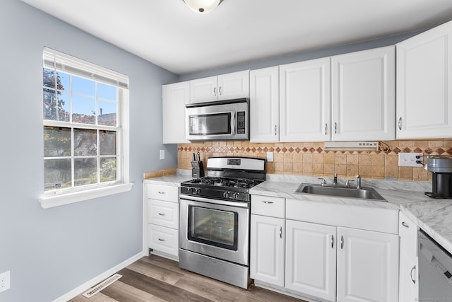 kitchen with decorative backsplash, stainless steel appliances, hardwood / wood-style floors, sink, and white cabinets