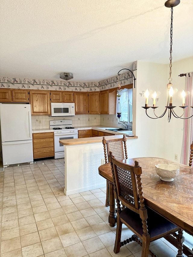 kitchen featuring kitchen peninsula, white appliances, sink, pendant lighting, and an inviting chandelier