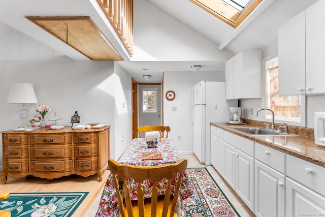 kitchen featuring sink, light wood-type flooring, white cabinets, lofted ceiling with skylight, and white refrigerator