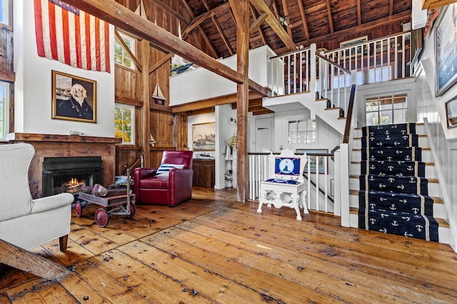 living room featuring high vaulted ceiling, wood walls, wood finished floors, a lit fireplace, and stairway