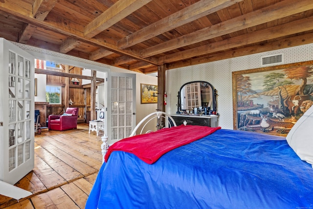 bedroom with wallpapered walls, beamed ceiling, french doors, light wood-style floors, and a fireplace