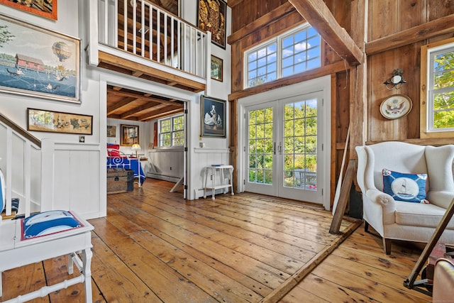 interior space featuring a wainscoted wall, wood finished floors, a towering ceiling, french doors, and baseboard heating