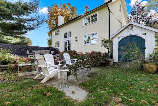 back of house with a yard, a patio area, an outdoor structure, and a chimney