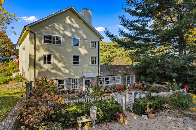 rear view of property featuring stone siding, fence, and a chimney