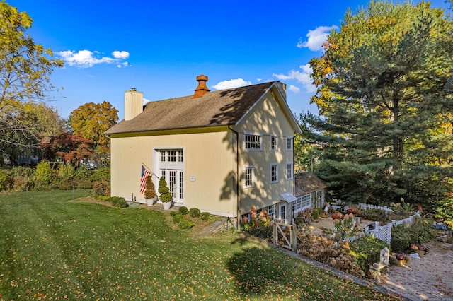 rear view of property featuring french doors, a lawn, a chimney, and an outdoor structure