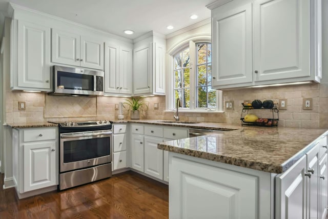 kitchen with stainless steel appliances, dark wood-style flooring, a sink, white cabinetry, and dark stone countertops