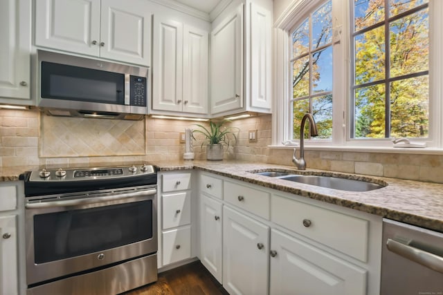 kitchen featuring appliances with stainless steel finishes, a sink, light stone counters, and white cabinets