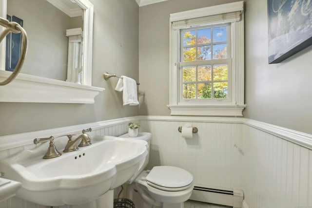 half bath with wainscoting, toilet, a sink, and baseboard heating