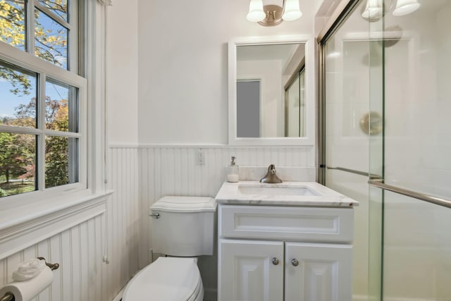 full bath featuring toilet, a wainscoted wall, a shower with door, and vanity