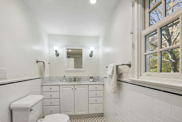 full bathroom featuring wainscoting, toilet, tile walls, and vanity