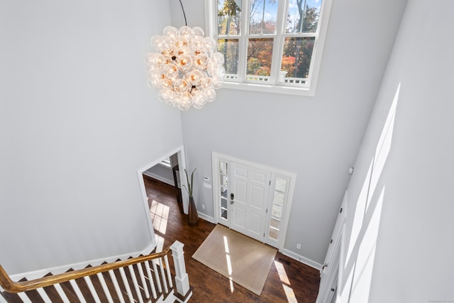 foyer entrance with dark wood-type flooring, a notable chandelier, and a towering ceiling