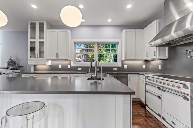 kitchen featuring wall chimney exhaust hood, stainless steel dishwasher, white cabinets, and decorative light fixtures