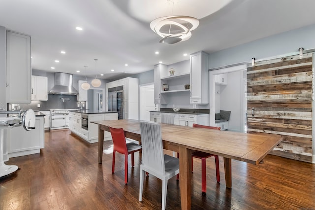 dining space featuring sink, dark wood-type flooring, a barn door, and wooden walls