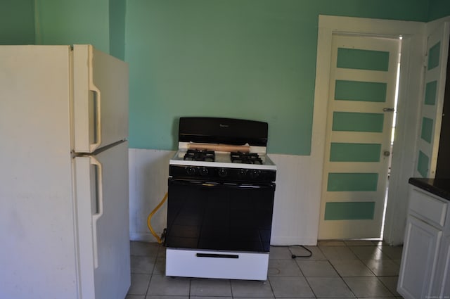 kitchen with white appliances, light tile patterned floors, tile counters, and white cabinets