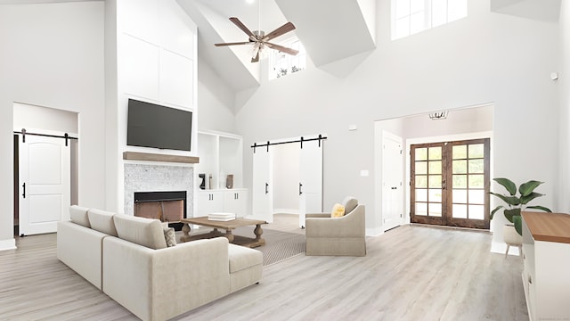 living room with a high ceiling, french doors, a barn door, a fireplace, and light hardwood / wood-style floors