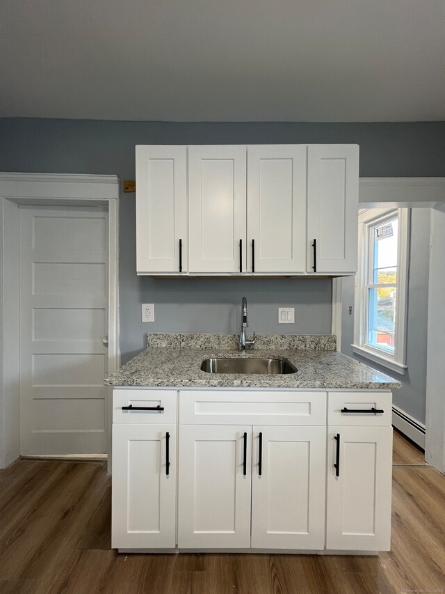 kitchen with light stone countertops, wood-type flooring, sink, and white cabinets