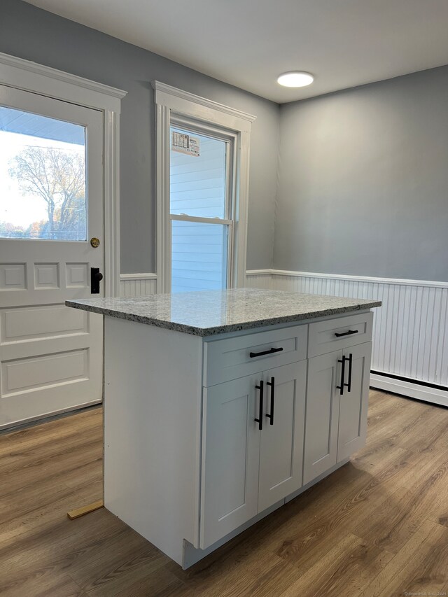 kitchen with white cabinets, light stone countertops, a center island, and wood-type flooring