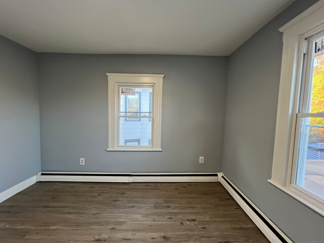 spare room featuring a baseboard heating unit and dark hardwood / wood-style flooring