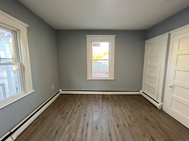 unfurnished bedroom with baseboard heating and dark hardwood / wood-style floors