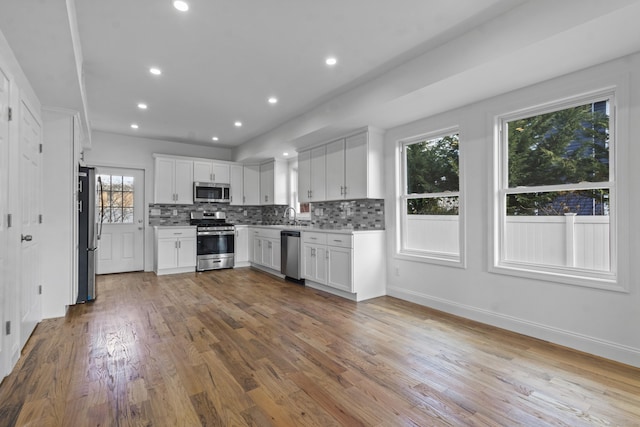 kitchen with a wealth of natural light, white cabinetry, backsplash, appliances with stainless steel finishes, and hardwood / wood-style flooring