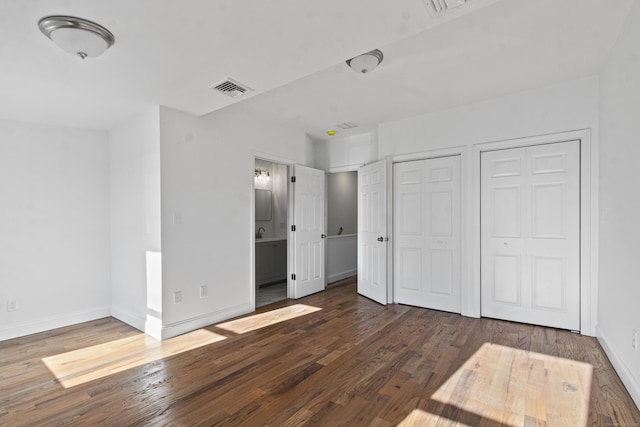 unfurnished bedroom with ensuite bathroom and dark hardwood / wood-style floors