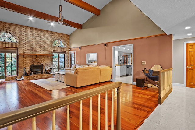 living room featuring ceiling fan, high vaulted ceiling, light wood-type flooring, beamed ceiling, and a fireplace