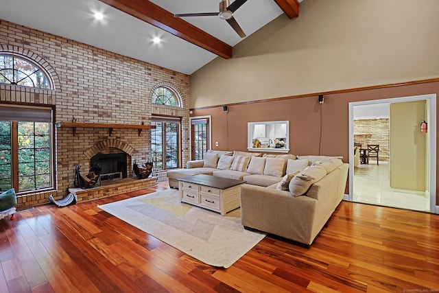 living room with hardwood / wood-style flooring, high vaulted ceiling, beamed ceiling, a fireplace, and brick wall