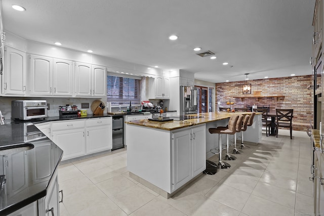 kitchen with brick wall, stainless steel fridge, a center island, and white cabinetry