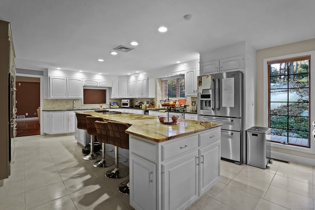 kitchen with white cabinetry, a breakfast bar, stainless steel refrigerator with ice dispenser, and a kitchen island