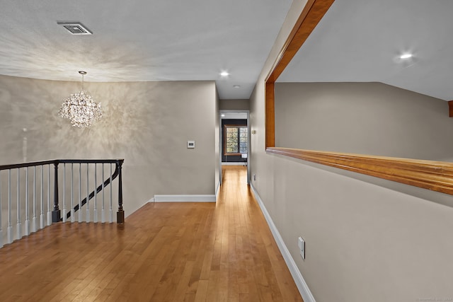 hallway with light hardwood / wood-style floors, a notable chandelier, and lofted ceiling