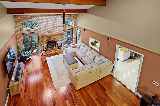 living room with beamed ceiling, hardwood / wood-style floors, high vaulted ceiling, and a brick fireplace