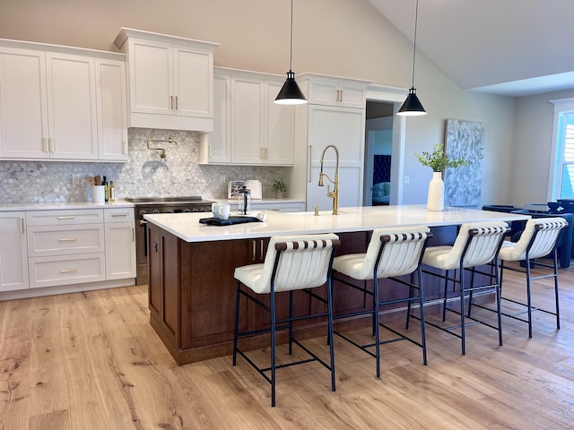 kitchen with a center island with sink, a kitchen breakfast bar, hanging light fixtures, stainless steel range, and white cabinetry